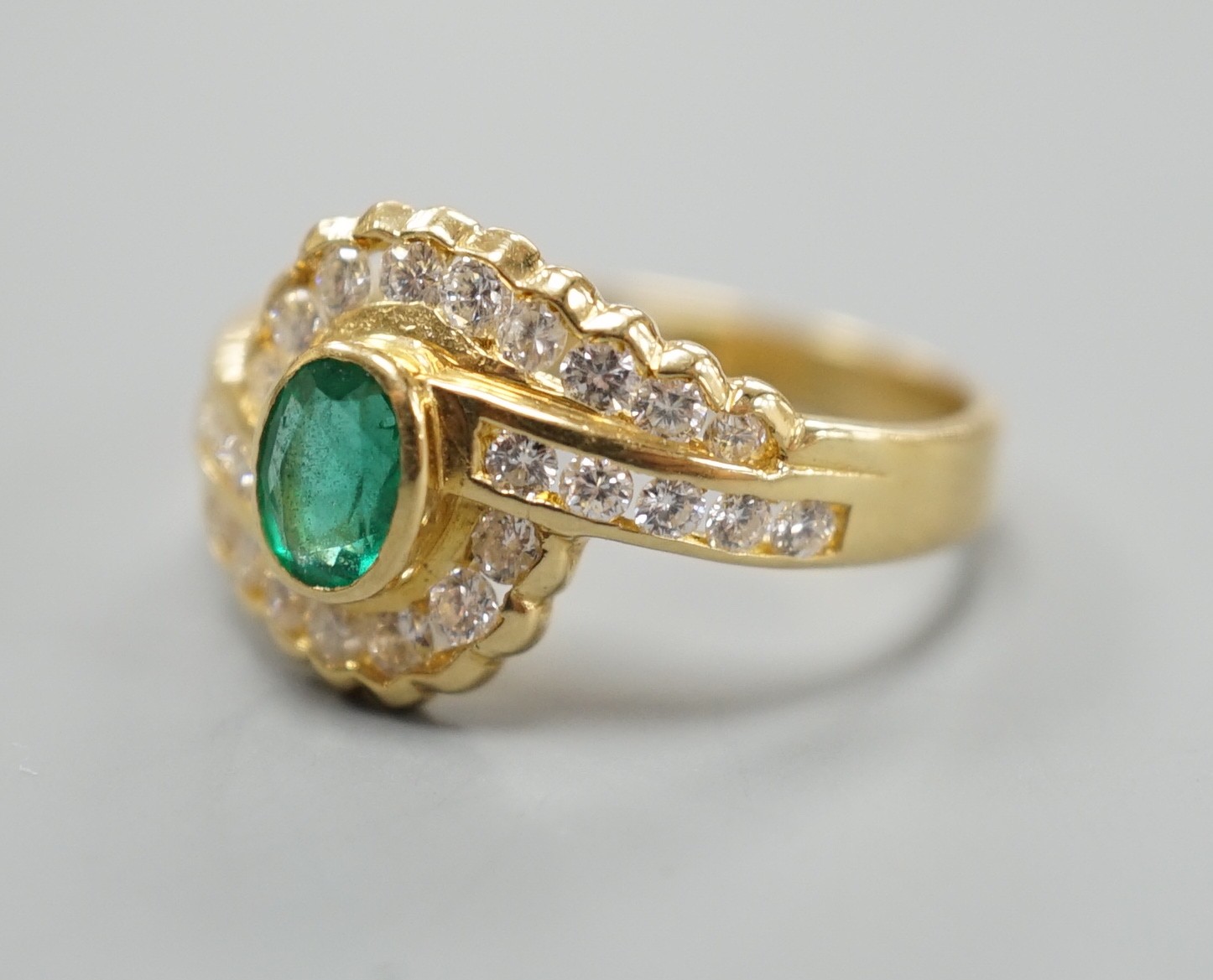 A modern 18ct gold, collet set oval cut emerald and diamond cluster set crossover ring, size N, gross weight 3.5 grams.